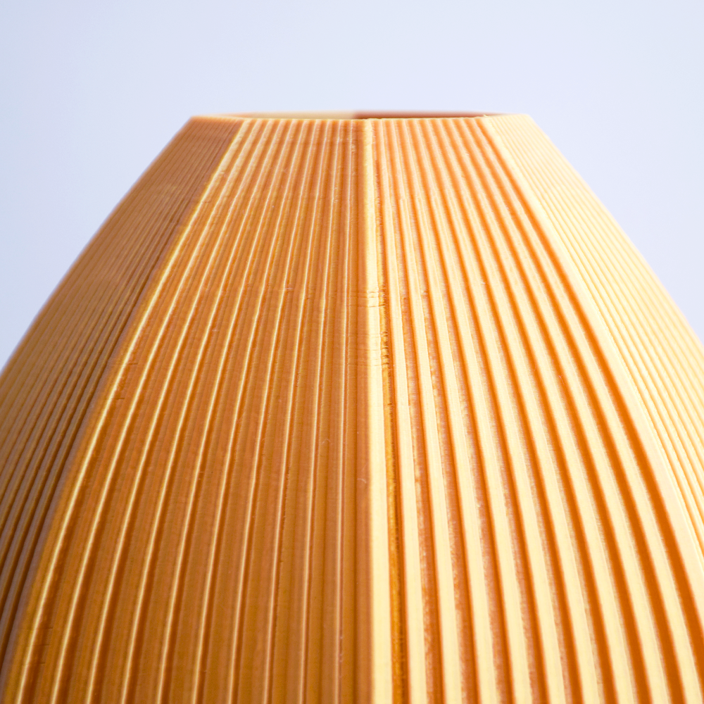 Close-up of a textured golden 3d print vase against a light blue background
