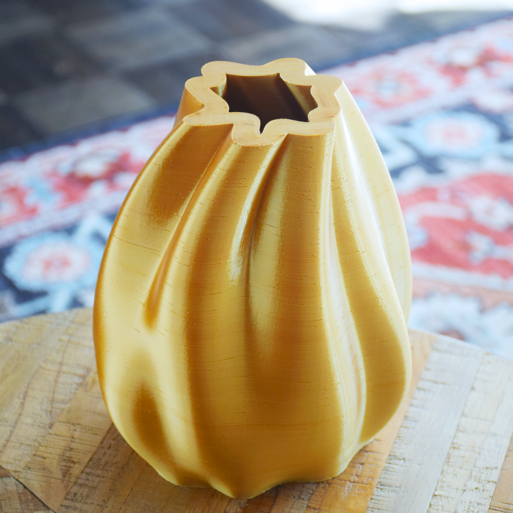Yellow 3D-printed vase on a woven surface with a blurred background