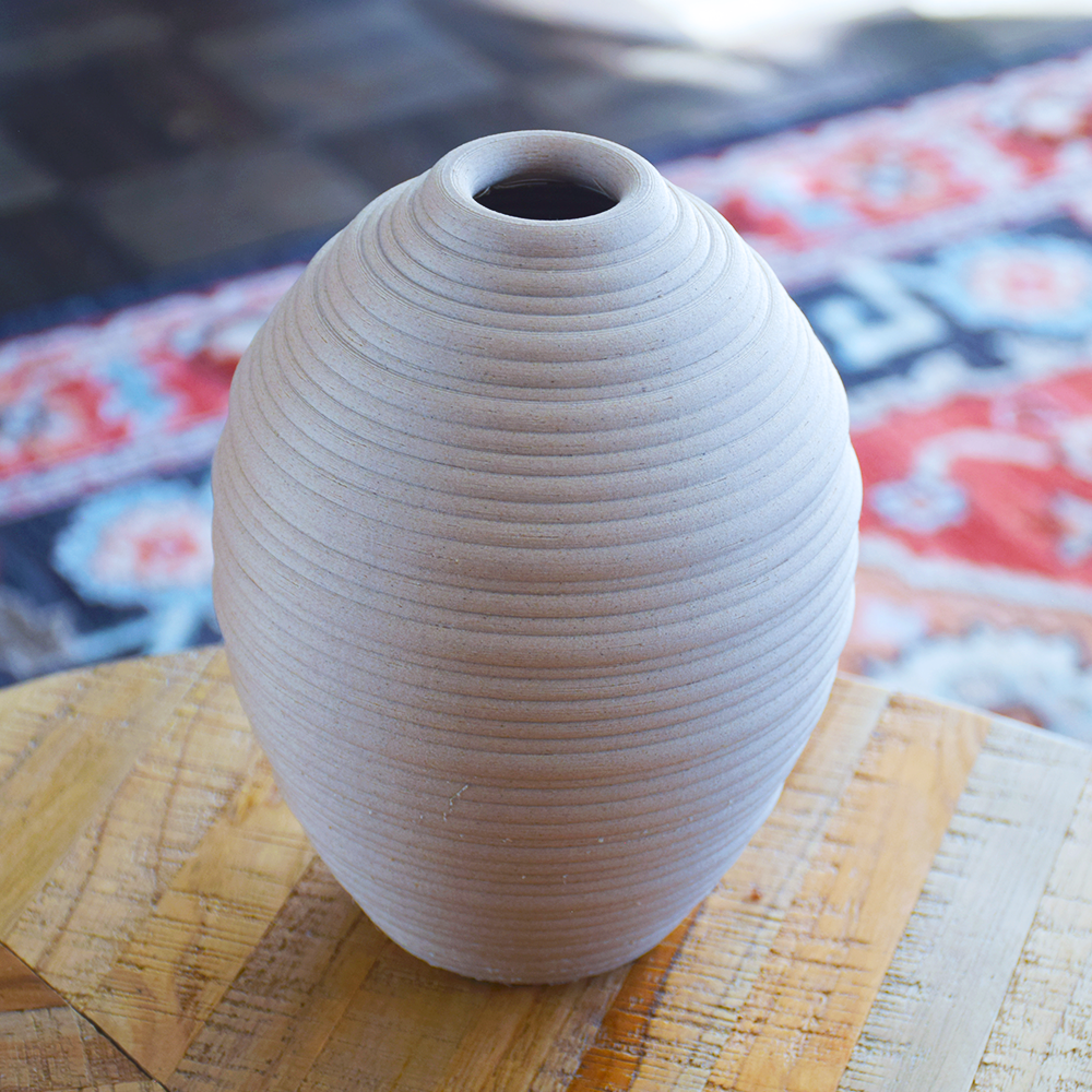 beige 3d print vase on a woven surface with a colorful patterned rug in the background