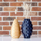 Two geometric-patterned vases, one gold and one blue, on a wooden surface with a light background.