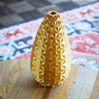 Yellow geometric-patterned vase on a textured surface with a colorful rug in the background